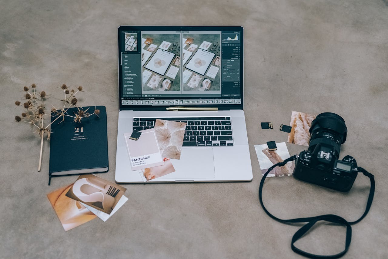 Overhead view of a photographer's workspace with a laptop, camera, and design prints.